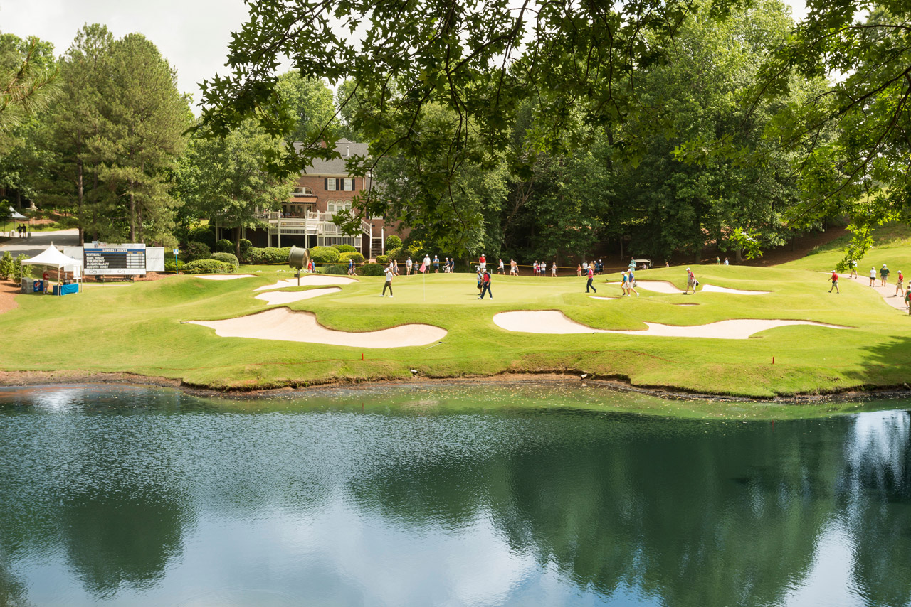 Golfers playing through on a pond-side green surrounded by sand traps at Thornblade Country Club. 
