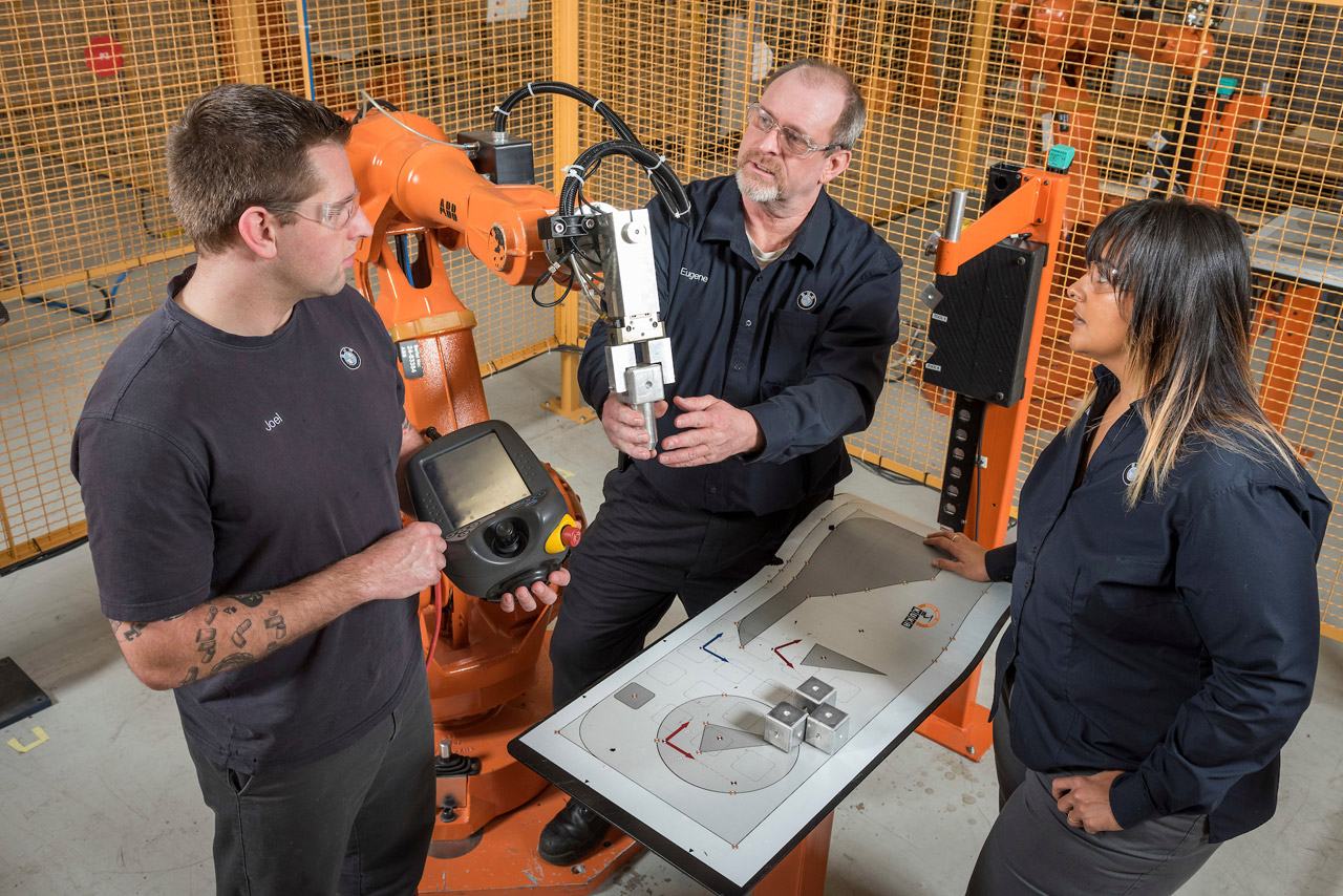 A supervisor teaches two BMW Scholars how to program a body shop robot. 